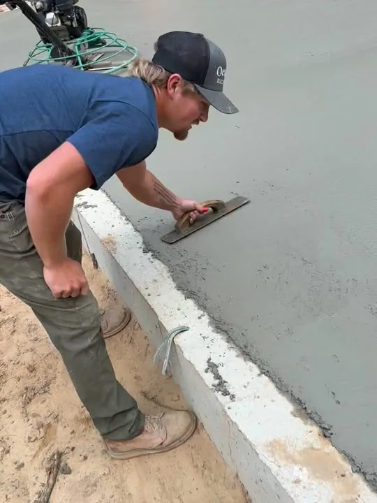 Crew member hand-troweling the edge of a fresh concrete slab